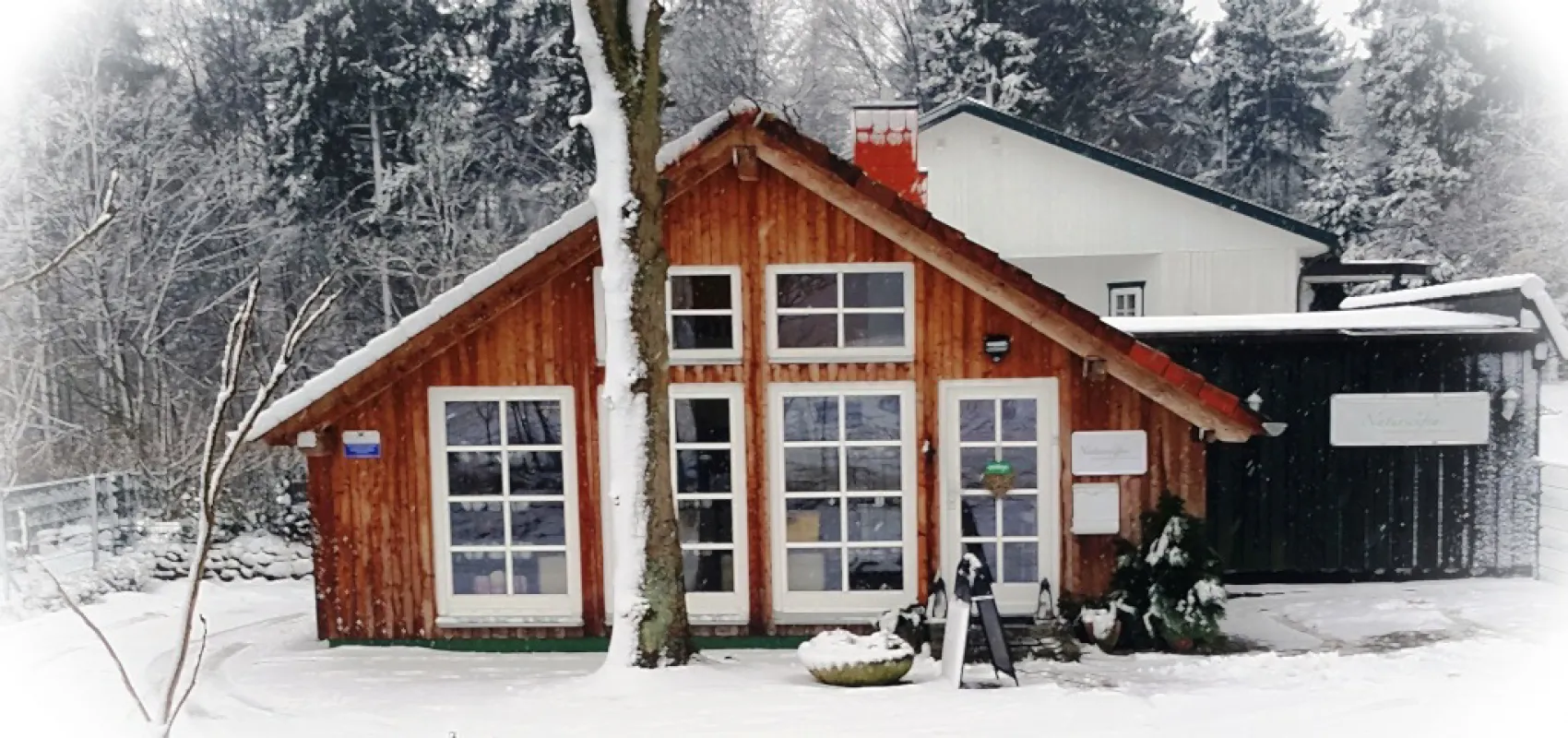 Gemütliches Holzhaus der Naturseifen-Manufaktur in winterlicher Landschaft. Schnee bedeckt das Dach und die Umgebung, während der Eingangsbereich einladend dekoriert ist.